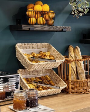 Un bufé de desayuno con cestas de pasteles, pan y naranjas.