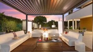 A covered outdoor seating area with white sofas, a wooden coffee table, and decorative items. - Villa Tiberio 6 2 Emma Villas (Genzano di Roma)