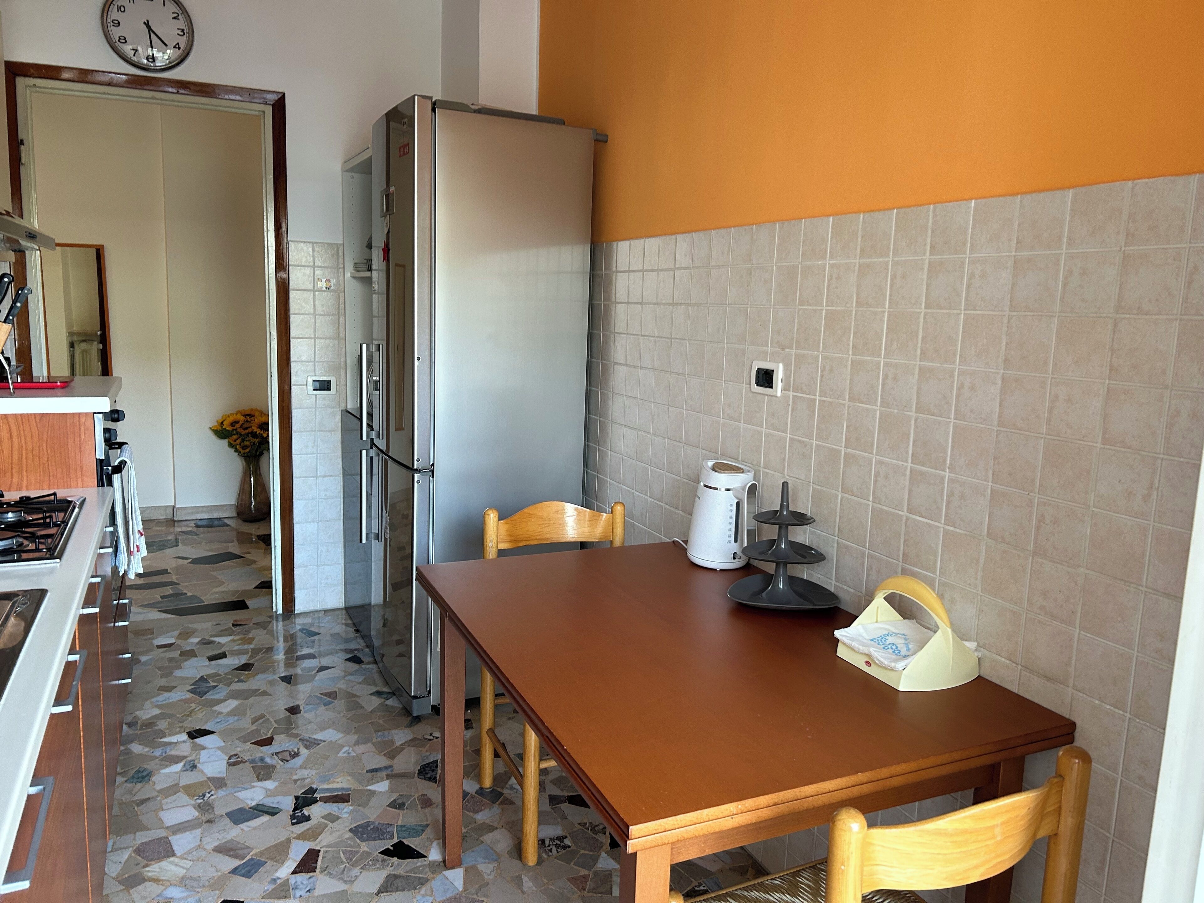 A kitchen with a tiled floor, a refrigerator, a stove, a sink, and a dining table with chairs.