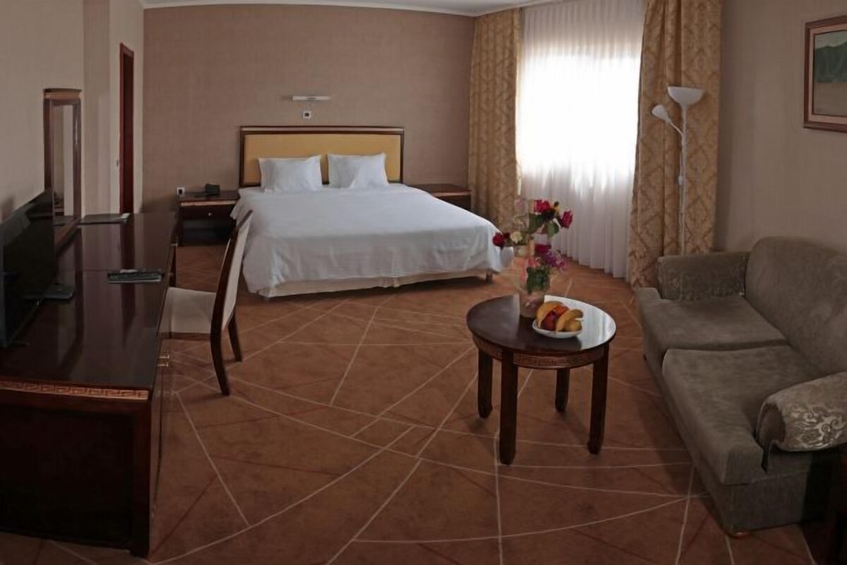 A hotel room with a bed, a desk, a sofa, and a small table with a vase of flowers.
