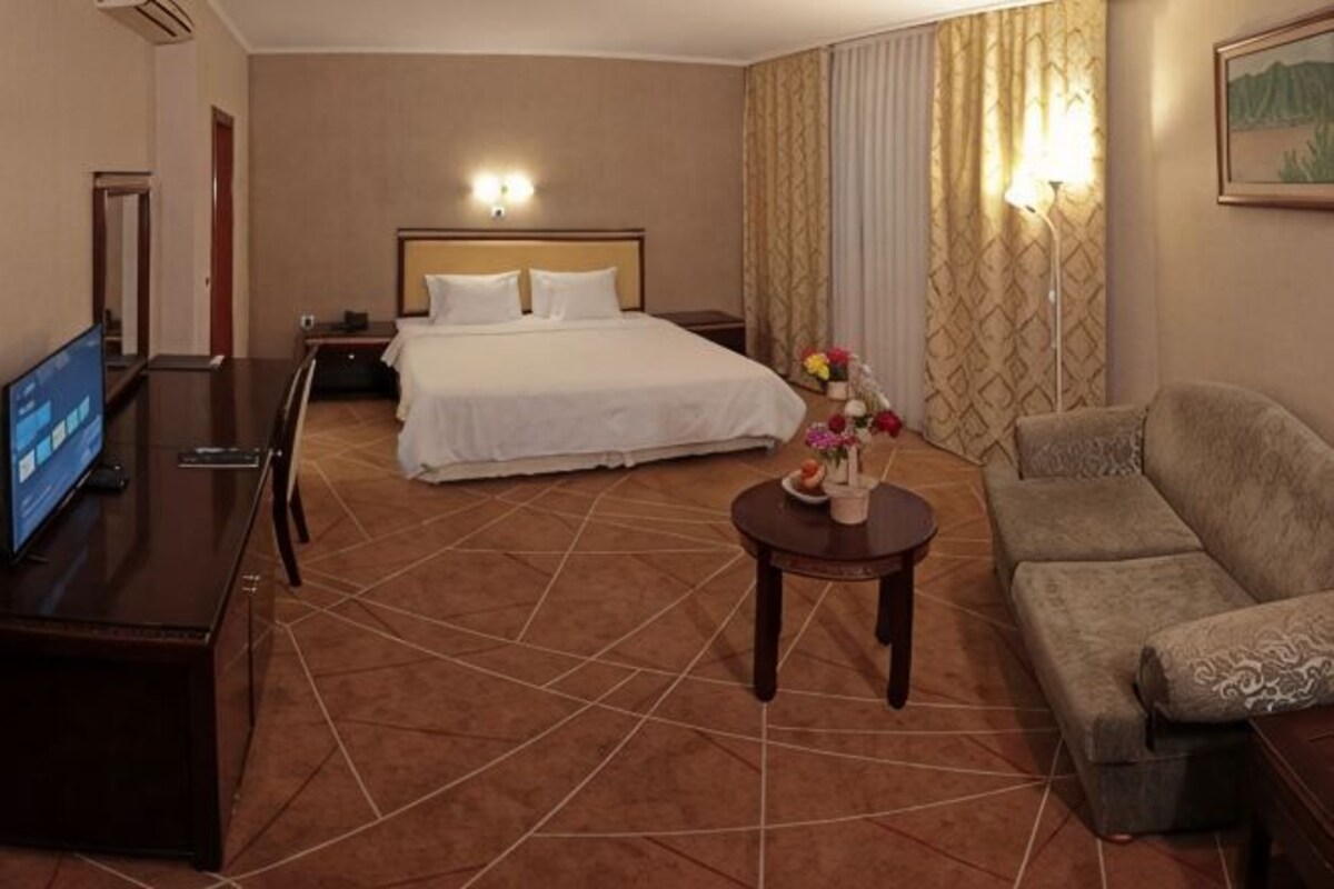Habitación de hotel con cama, televisor, sofá, una mesita con flores y lámpara.