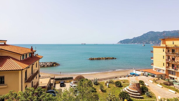 Une vue côtière avec des bâtiments, une plage et un promontoire rocheux dans la mer.