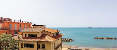 A coastal building with a tiled roof overlooking a beach and the sea.