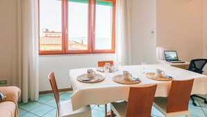 Un coin repas avec une table dressée pour quatre personnes, un ordinateur portable posé sur un bureau et une vue sur des immeubles par la fenêtre.