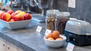 Una barra de desayuno con tazones de fruta, nueces y huevos, además de una máquina de café.