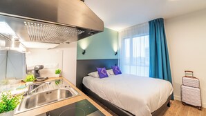 Una habitación de hotel moderna con cama, kitchenette y maleta.