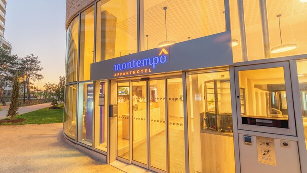 Entrada de un moderno hotel-apartamento con puertas de vidrio y un letrero que dice "montempo APPORTHOTEL".