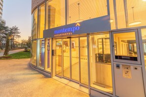 Der moderne Eingang eines Apartmenthotels mit Glastüren und einem Schild mit der Aufschrift 'montempo APPORTHOTEL'.