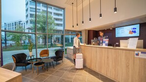 Zona de recepción de un hotel con un ventanal grande, un mostrador de recepción y un área de descanso con sillas y una mesa.