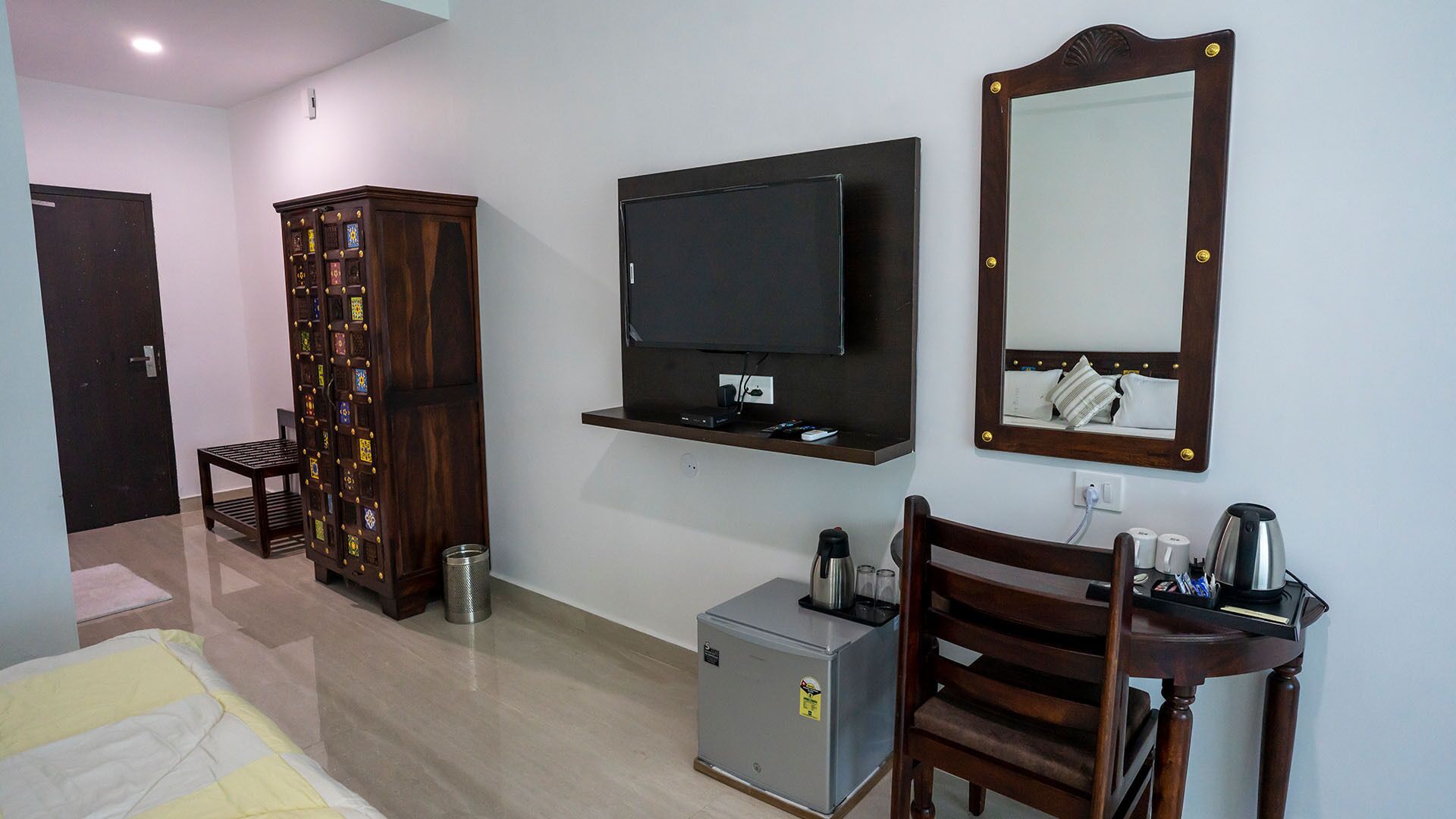 Une chambre d’hôtel comprenant un lit, une télévision, un miroir, une petite table avec une bouilloire, une armoire et une poubelle.