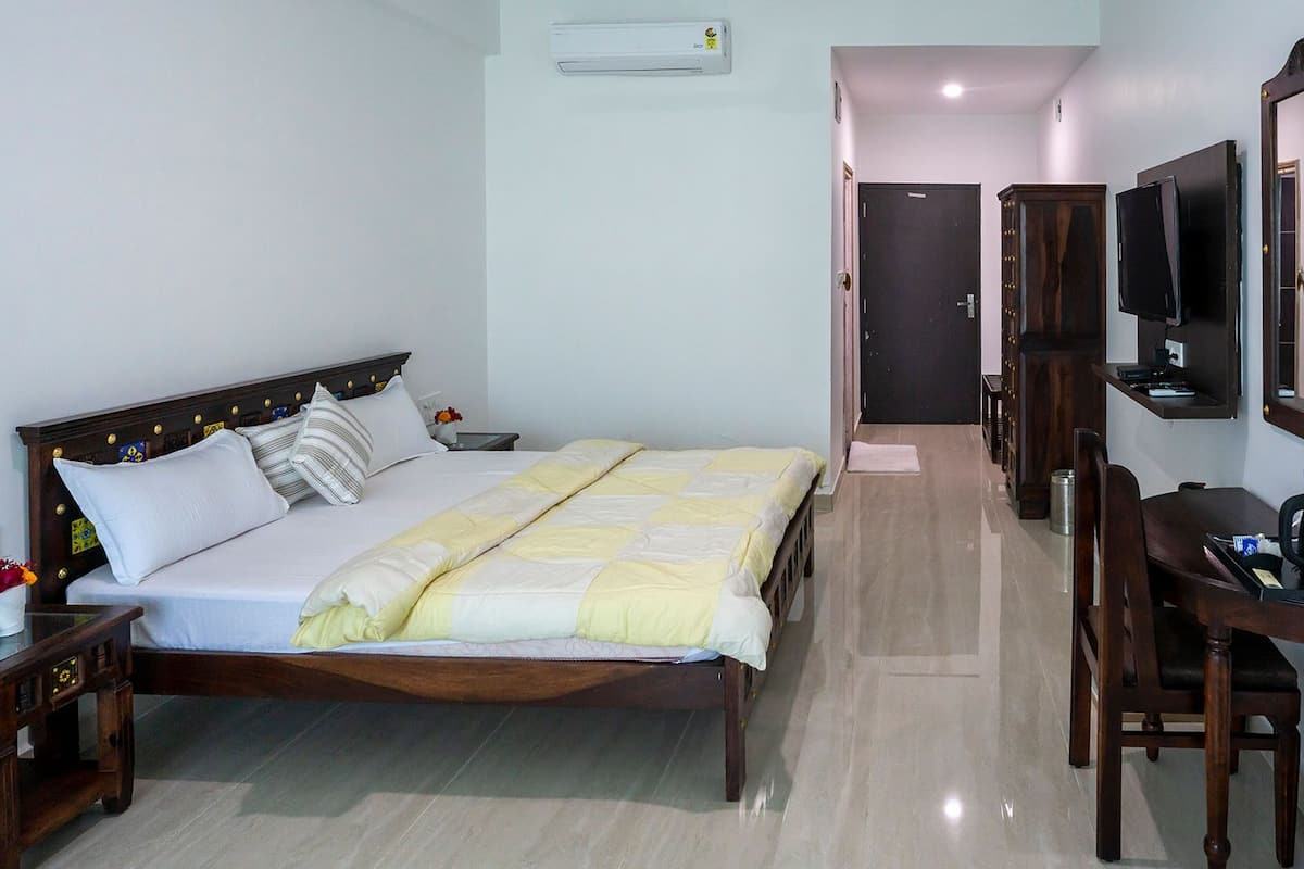Una habitación de hotel ordenada con cama, mesita de noche, escritorio con silla, espejo y aire acondicionado de pared.