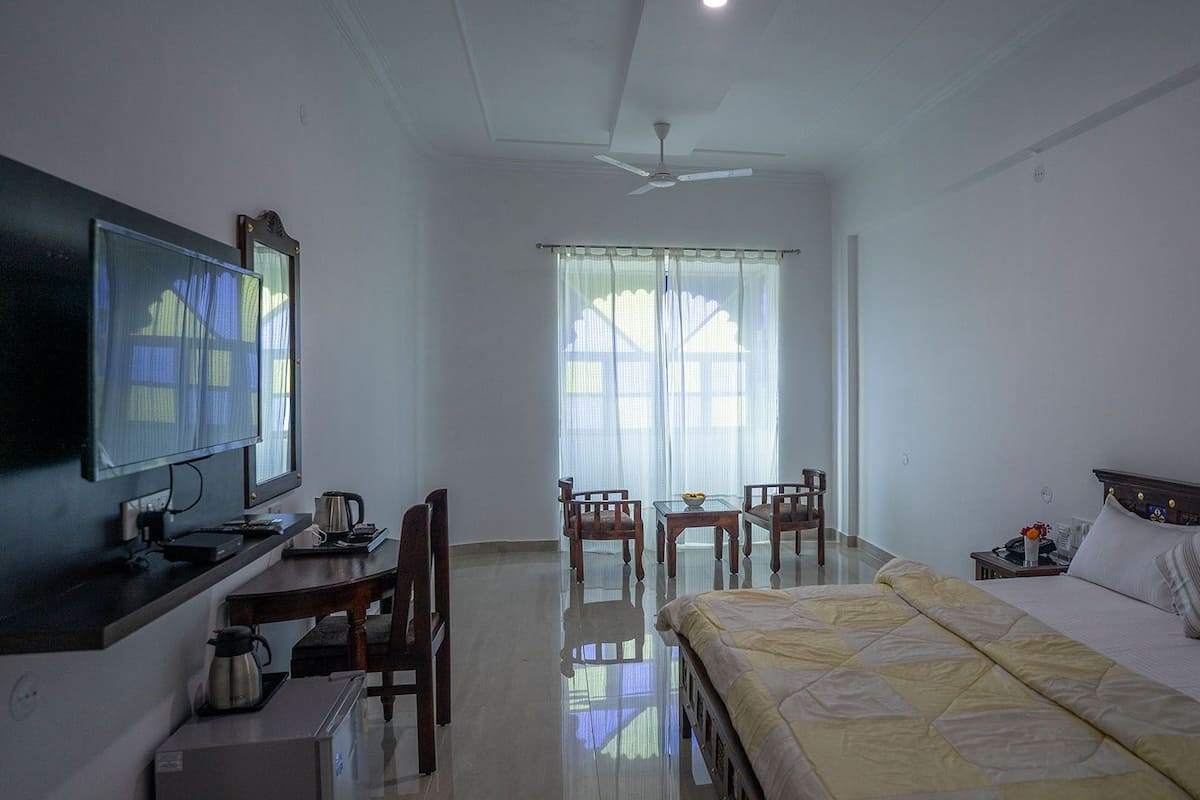Habitación de hotel con cama, escritorio con televisor, cafetera y zona de comedor con sillas y mesa.