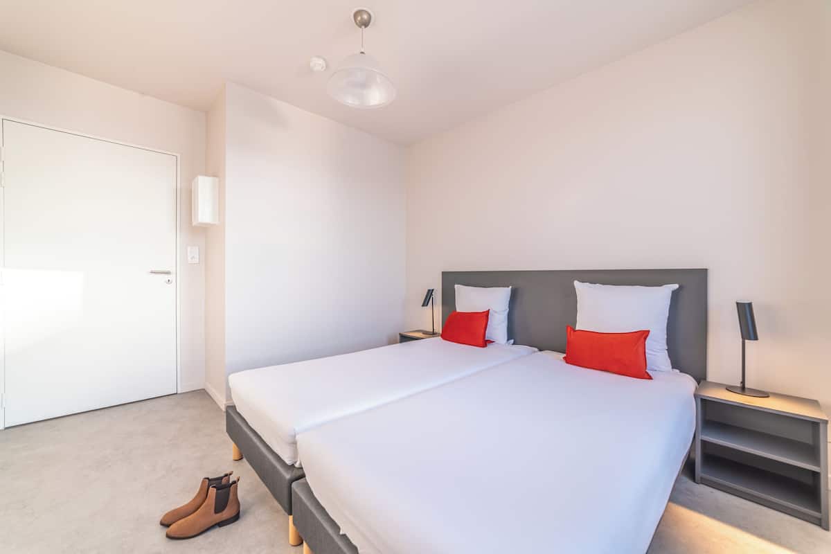 A modern hotel room with a large bed, two bedside tables, a wardrobe, and a door.