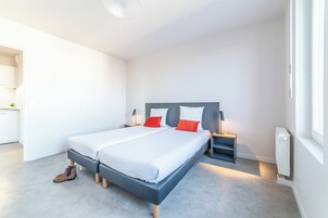 Un dormitorio moderno con una cama grande, mesitas de noche, un radiador y vistas a la cocina contigua.