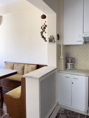 A compact kitchen with a built-in stove, a small refrigerator, and a microwave. There's a wooden dining table with chairs and a white partition. - The Observatory 2BR With Acropolis View (Athens)