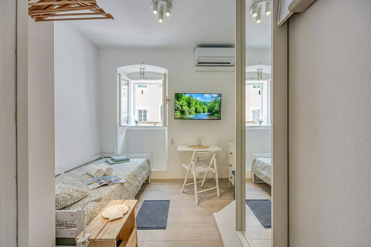 A compact bedroom with a bed, a small desk, a chair, and a TV on the wall.