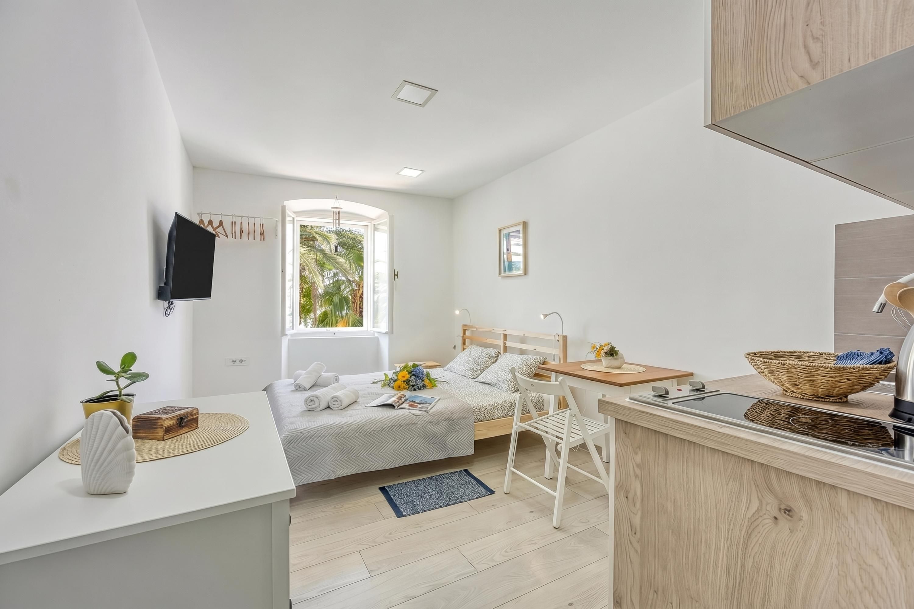 Habitación de hotel compacta con cama, un escritorio pequeño, kitchenette y ventana con vista a follaje.