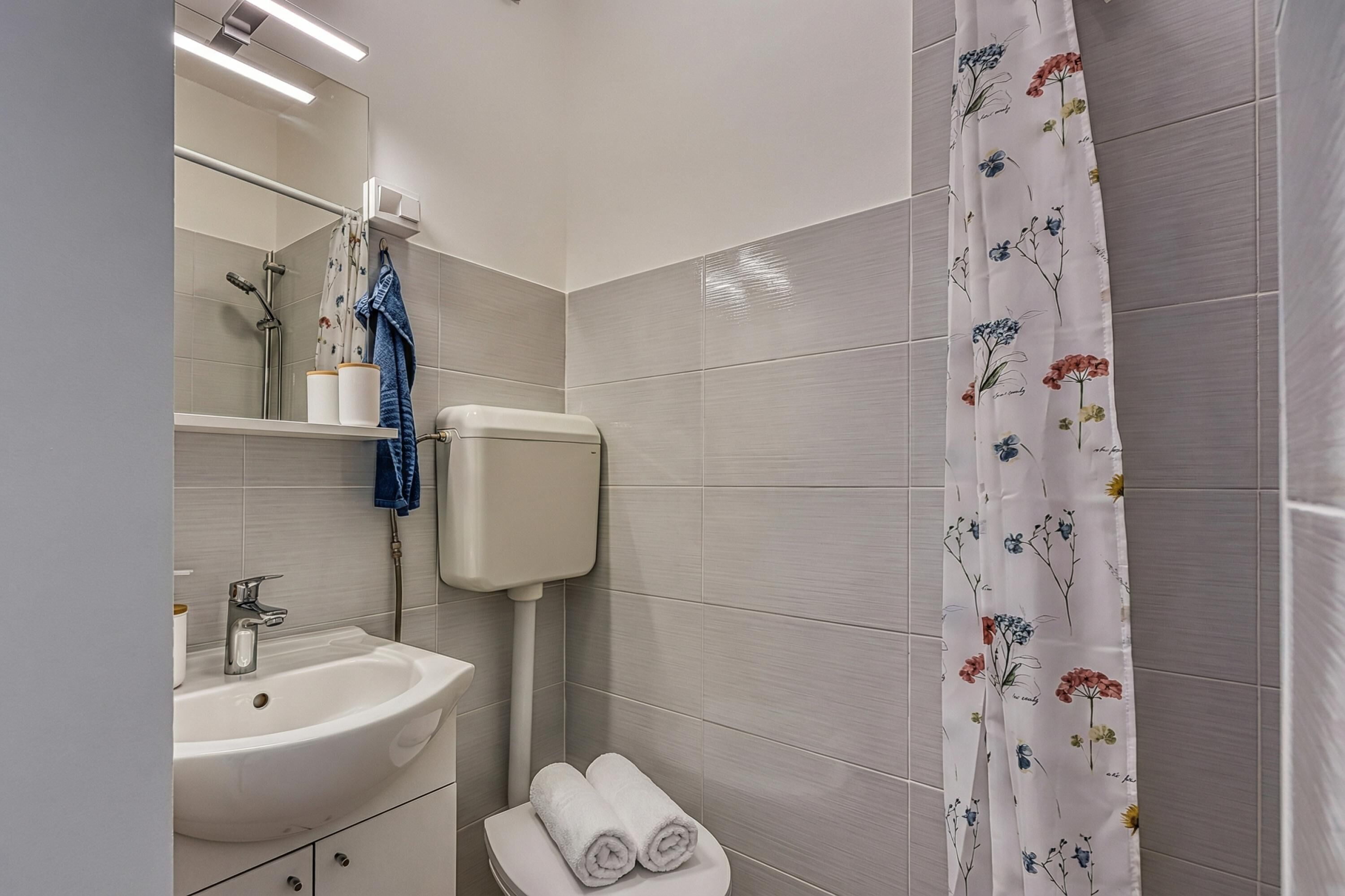 Une salle de bain équipée d’un lavabo, d’un miroir, de toilettes et d’un rideau de douche.