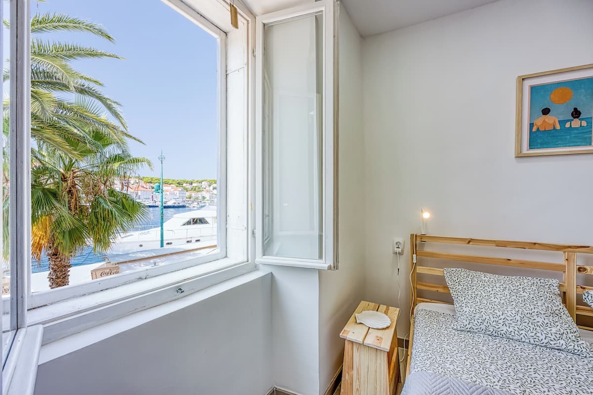 A bedroom with a wooden bed, a window with a view of a marina, and a framed painting on the wall.