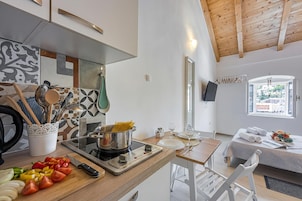 Una cocina moderna con estufa, tabla de cortar y utensilios. Se ve un comedor con mesa y sillas.