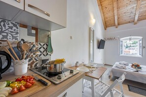 A modern kitchen with a stove, cutting board, and utensils. A dining area with a table and chairs is visible.