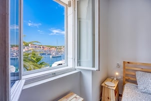 Un dormitorio con vistas al puerto, una mesita de noche de madera con una lámpara y una cama con un cojín estampado.