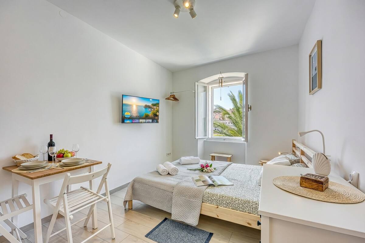 A bedroom with a bed, a desk with a chair, a window, and a painting on the wall.