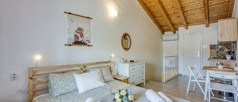 Een slaapkamer met een houten plafond, een bed met beddengoed met een patroon, een nachtkastje, een wandspiegel en een klein bureau met een stoel.
