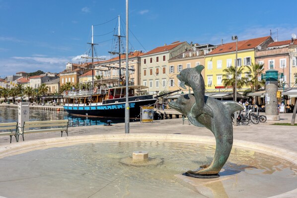 A public square with a fountain, benches, and a boat docked by the water.