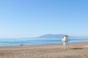 A lifeguard tower on a beach with clear skies and mountains in the background.
