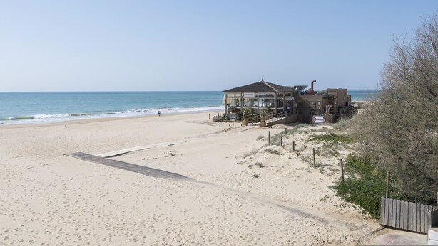 Ein Gebäude direkt am Strand mit einer überdachten Terrasse, neben einem Sandstrand und dem Meer.