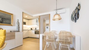 Eine moderne Küche mit weißen Schränken, ein Essbereich mit Korbstühlen und eine Statue an der Wand.