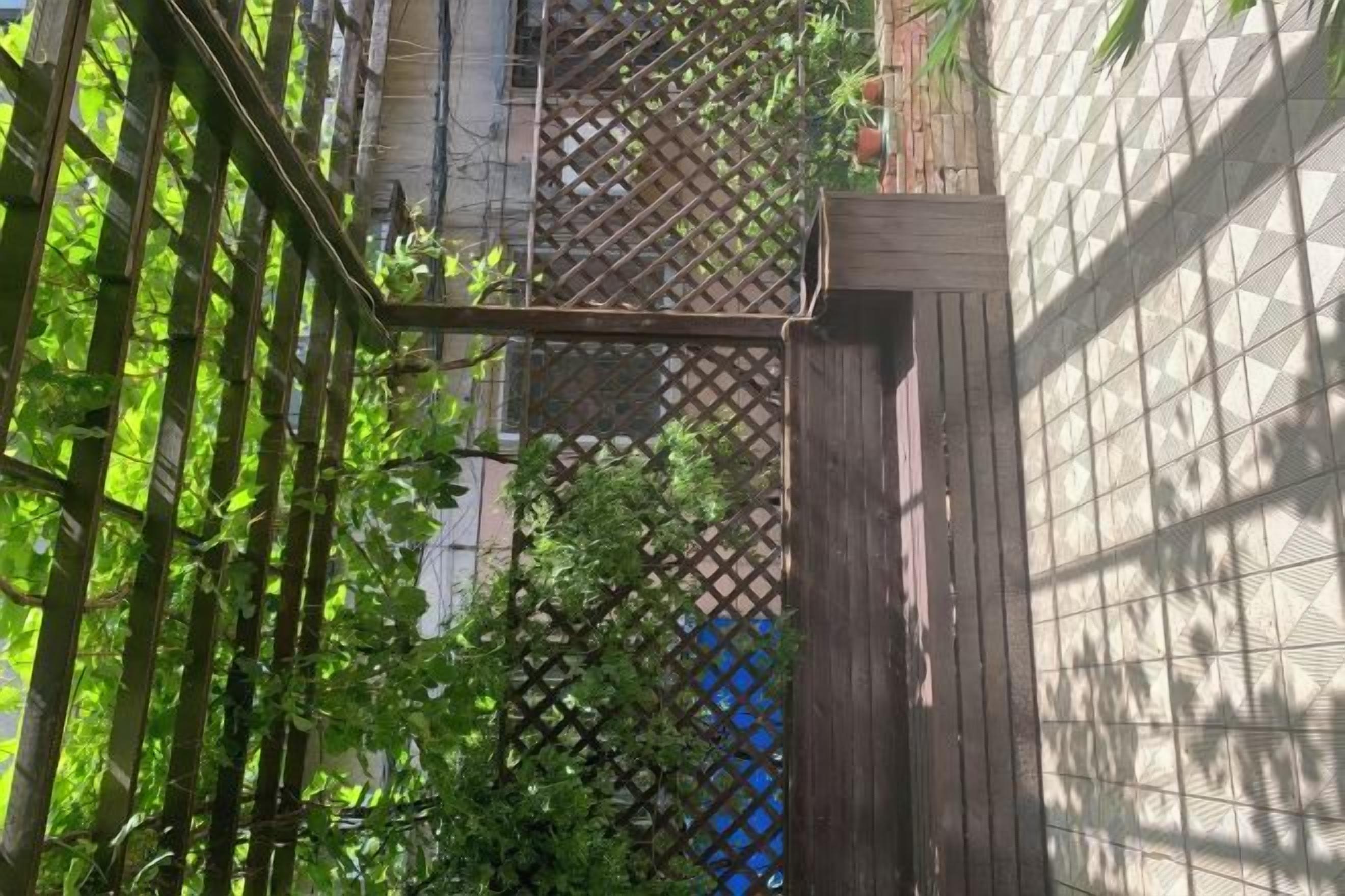 A narrow alleyway with a wooden gate, a lattice fence, and a building with a geometric patterned facade.