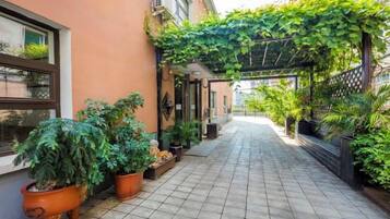 A narrow, tiled pathway flanked by potted plants and a building with a covered entrance.
