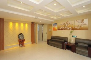 A reception area with a reception desk, two sofas, a wall-mounted clock, and a door leading to another room. - Changji Express Hotel (Liaoyang)
