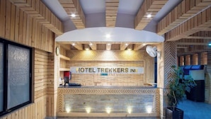 Een receptiebalie met een bord waarop 'HOTEL TREKKERS INN' staat, en een modern interieur met houten lambrisering en een geblokt patroon op de muren.