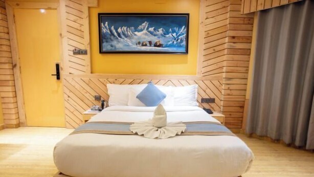 Een hotelkamer met een houten hoofdeinde, een bed met een wit en blauw beddegoed, een schilderij van een besneeuwd berglandschap en een houten vloer.