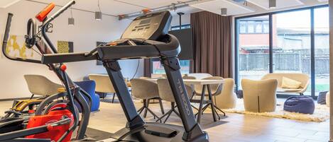 A gym with a treadmill, stationary bike, and rowing machine. There are chairs and a table in the background.