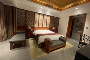 A hotel room with a bed, two bedside tables, a chair, a desk, and a decorative wall panel.