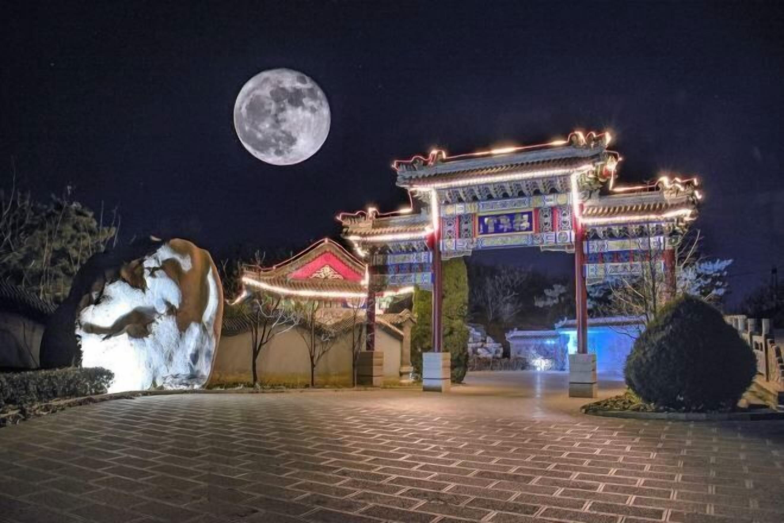 A traditional Chinese gate illuminated at night with a full moon in the background.
