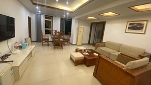 A modern living room with a sofa, coffee table, TV, and a dining area with chairs and a table. - Fuquan Xingong Hot Spring Resort (Zunhua)