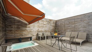 Une terrasse en bois avec un jacuzzi, des sièges d’extérieur et une table avec des boissons.