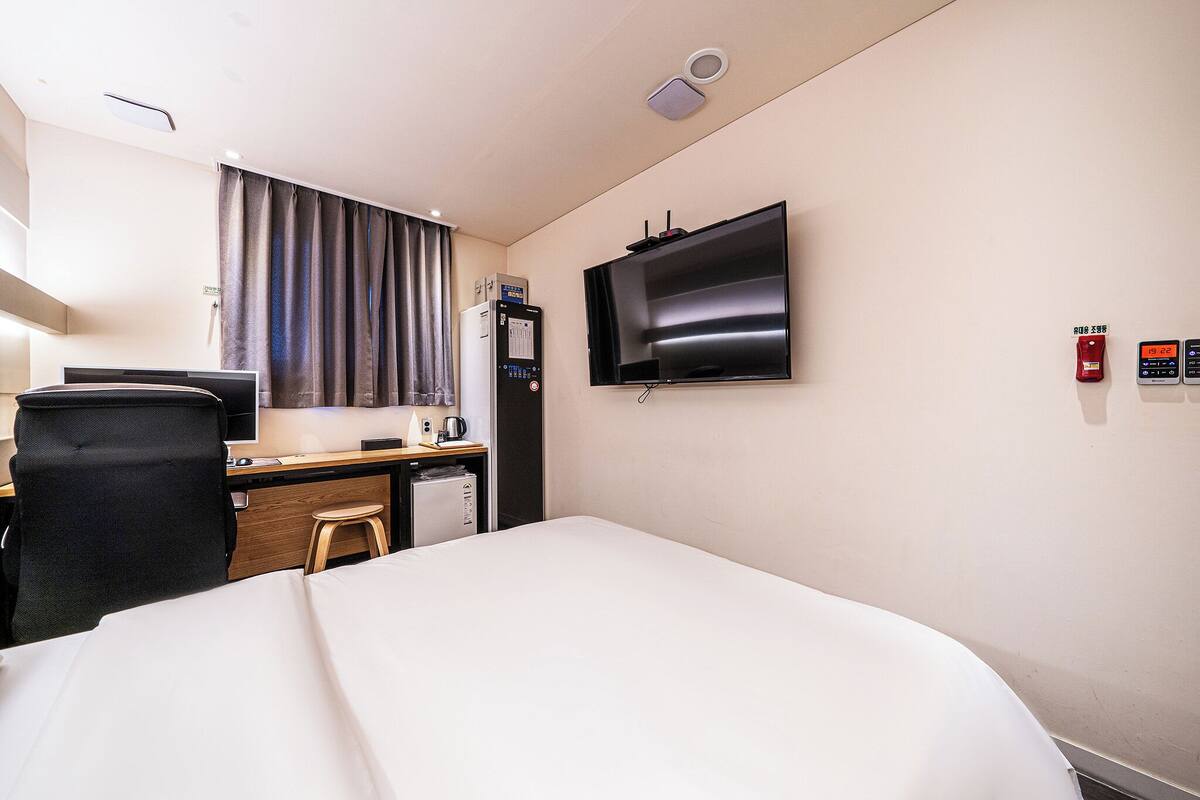 Ein Hotelzimmer mit einem Bett, einem Schreibtisch mit Computer, einem Fernseher und einer kleinen Küchenzeile.