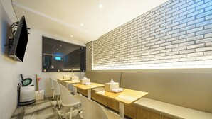 Un restaurant moderne avec un mur en briques, des tables en bois, des chaises blanches et un téléviseur fixé au mur.