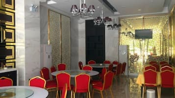 A dining area with round tables and red chairs, a chandelier, and a patterned wall.