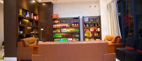 A modern hotel lobby with a central seating area, a large bookshelf, and a view of the city.