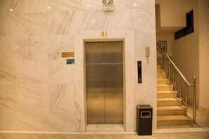 An elevator with a sign, a trash bin, and a staircase with a handrail. - Nanuo Holiday Hotel (Sanya)