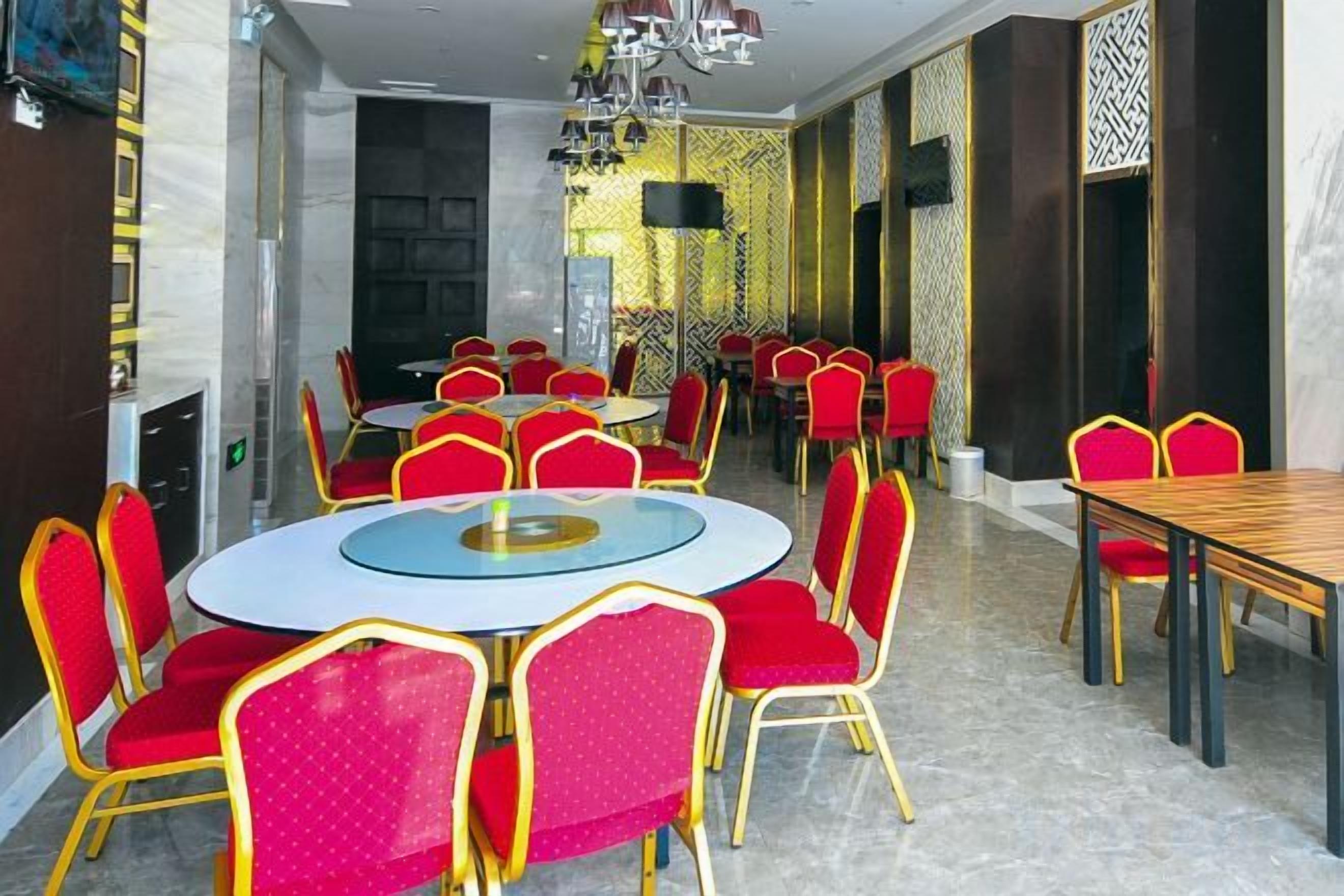 Un espace repas avec des tables rondes et des chaises rouges, une cheminée et des murs à motifs.