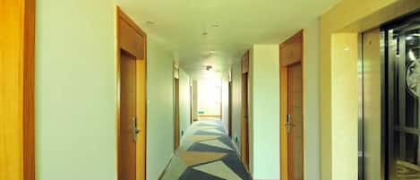 A hotel corridor with doors on both sides, a patterned carpet, and an elevator on the right.