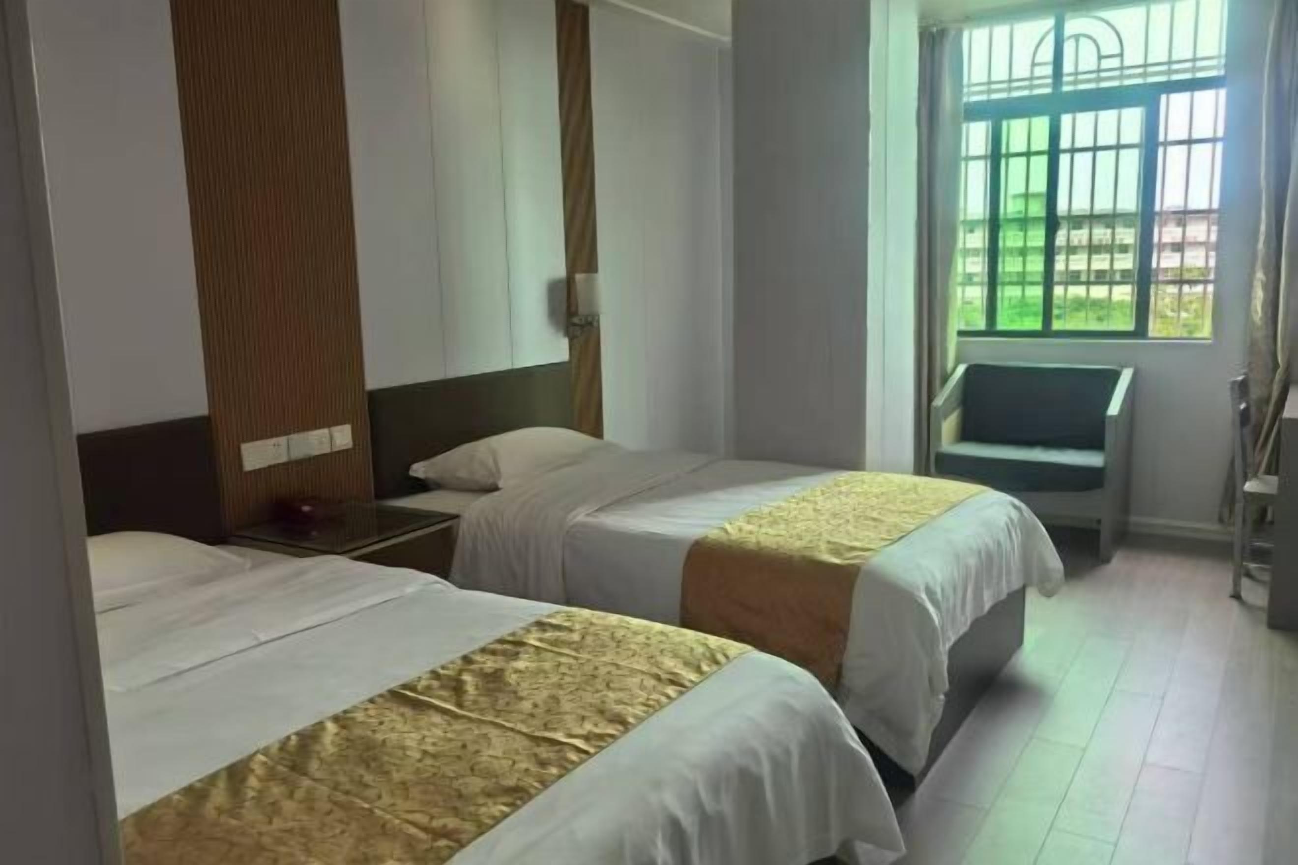 Habitación de hotel con dos camas, una mesita de noche, una silla y una ventana con barrotes.